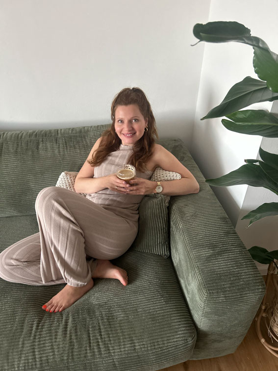 Firmeninhaberin und Copywriterin Eva Beksa, sitzt auf einem grünen Sofa und trinkt Kaffee. Das Foto ist aus der Vogelperspektive gemacht.